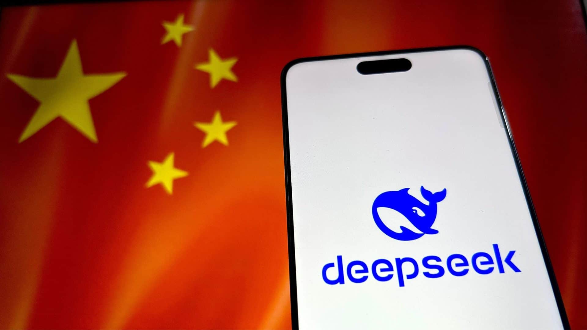 Celular com logotipo da DeepSeek na tela colocado na frente de monitor exibindo bandeira da China