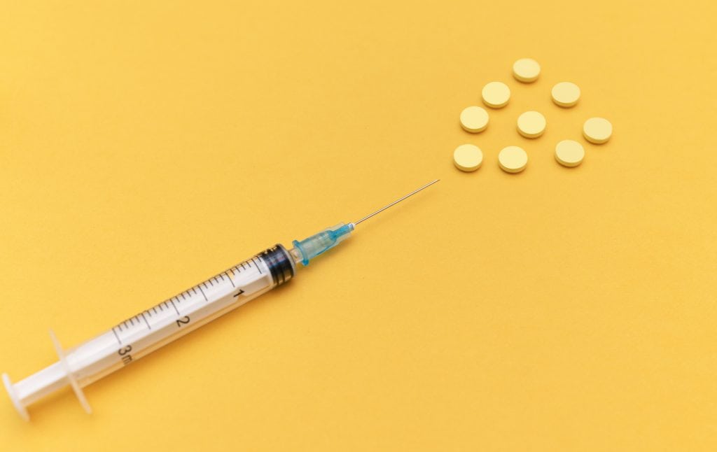 seringa e comprimidos em fundo amarelo