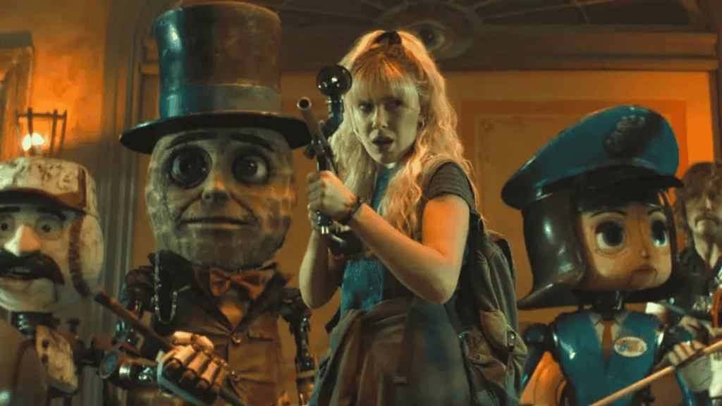 Uma mulher loira armada ao lado de bonecos humanoides em um cenário iluminado