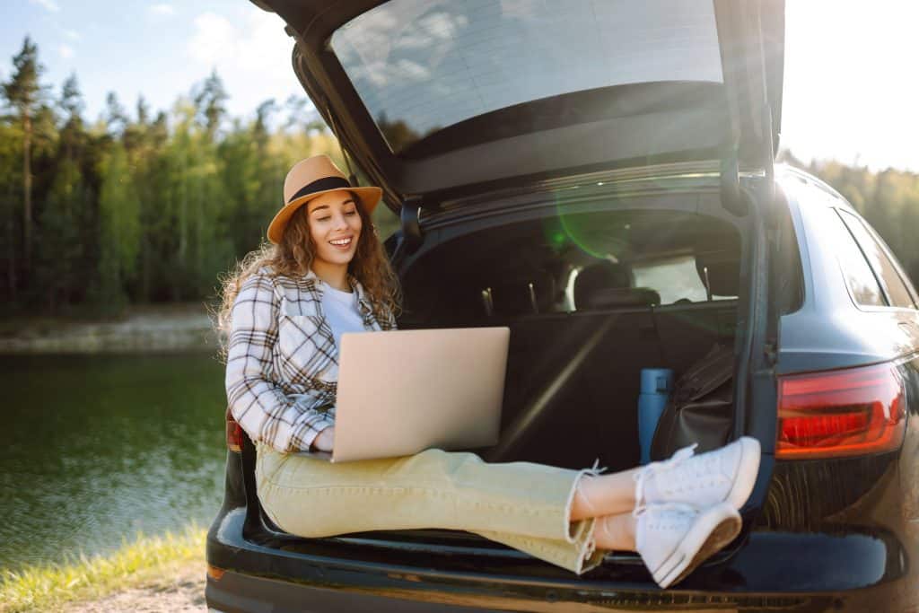 Imagem mostra mulher usando laptop sentada na parte de trás de um carro, para evitar quedas e arranhões com notebook é preciso ter cuidado no transporte e manuseio