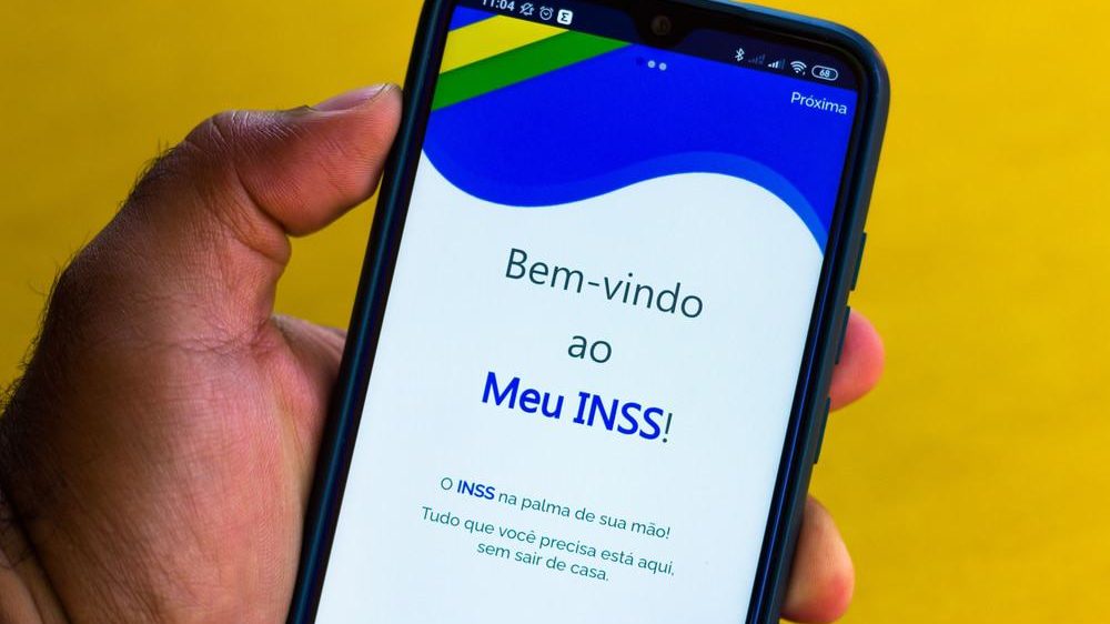 Pessoa segurando celular com aplicativo Meu INSS aberto na tela inicial