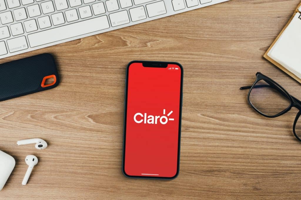 Claro, empresa de telecomunicações, aplicativo na tela do smartphone em fundo de madeira com um computador ao lado.