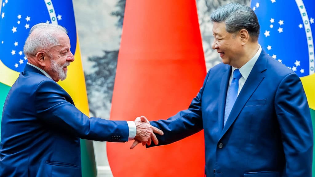 Lula apertando a mão de Xi Jinping na frente de bandeiras do Brasil e da China