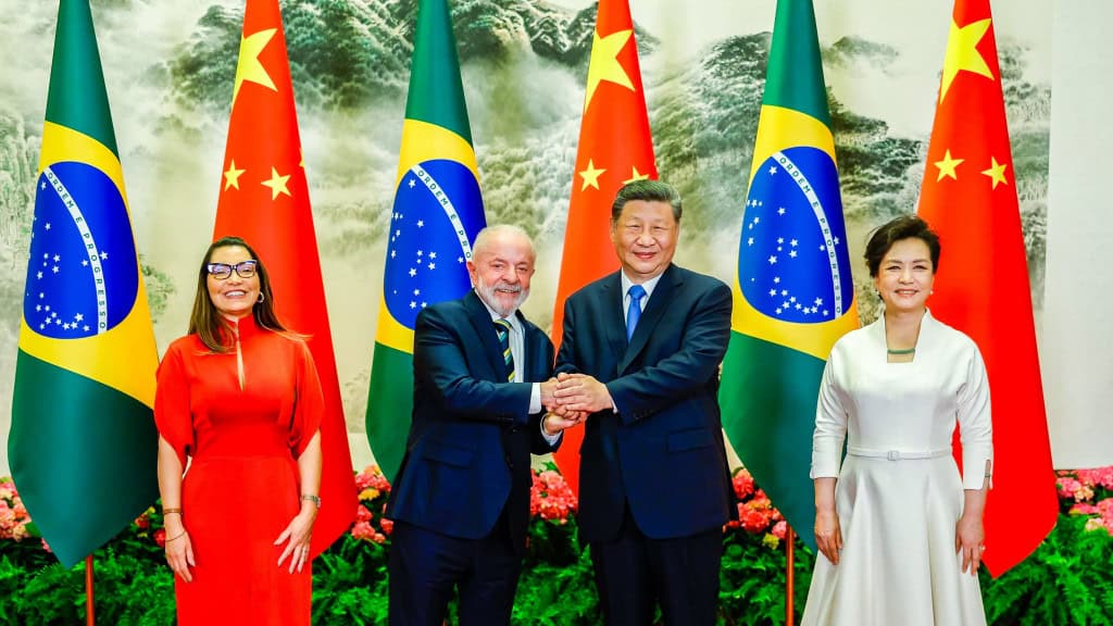 Lula e Xi Jinping ao lado de suas respectivas esposas na frente de bandeiras do Brasil e da China