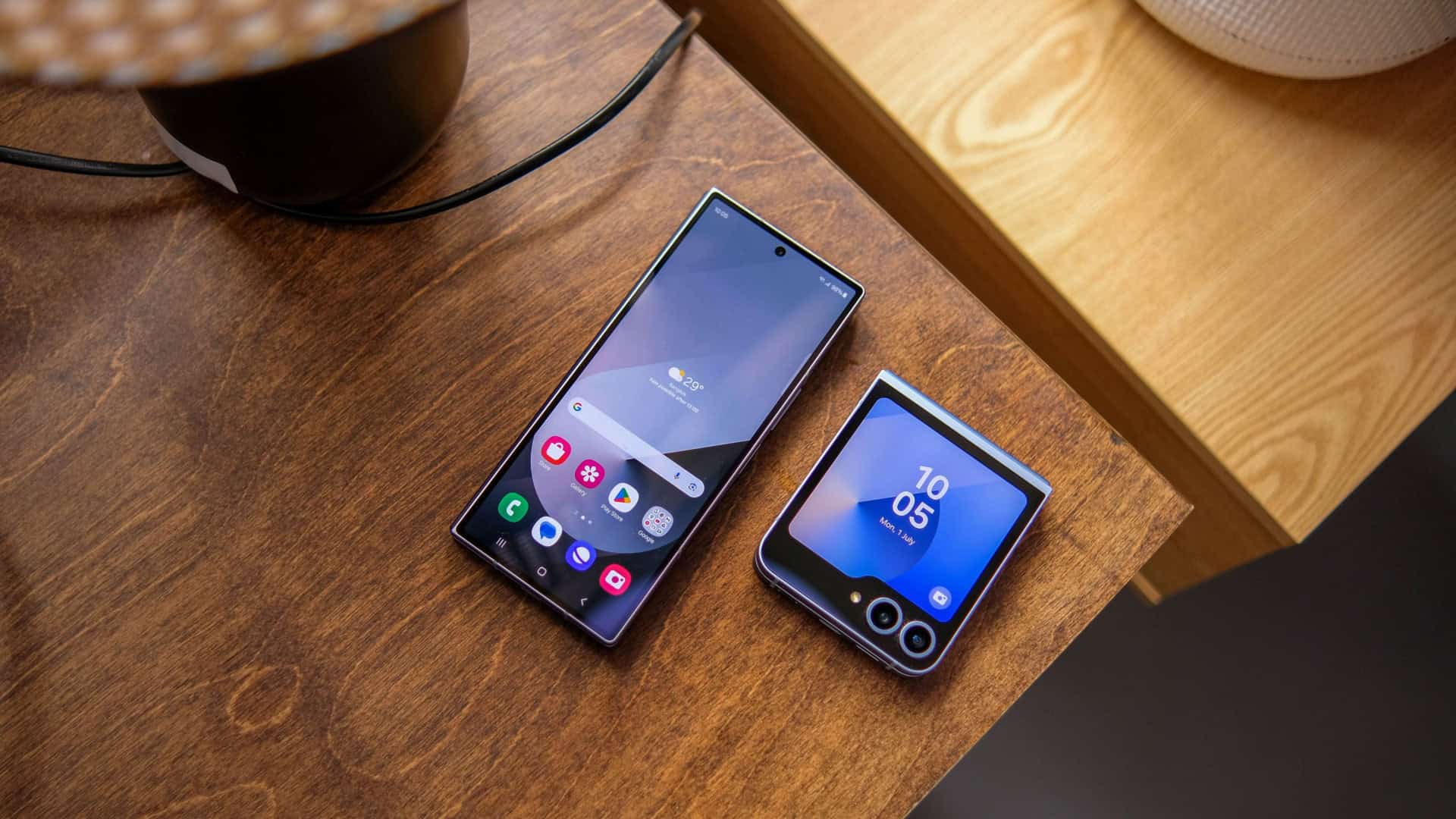 Galaxy Z Fold 6 e Galaxy Z Flip 6 em cima de mesa de madeira com telas acesas mostrando One UI