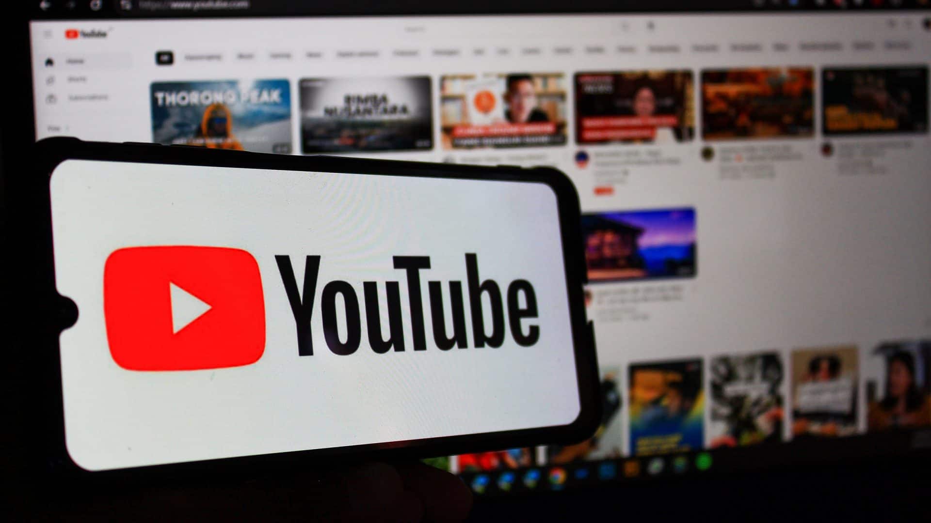 À frente, logo do YouTube em um smartphone; atrás, página do YouTube em um notebook