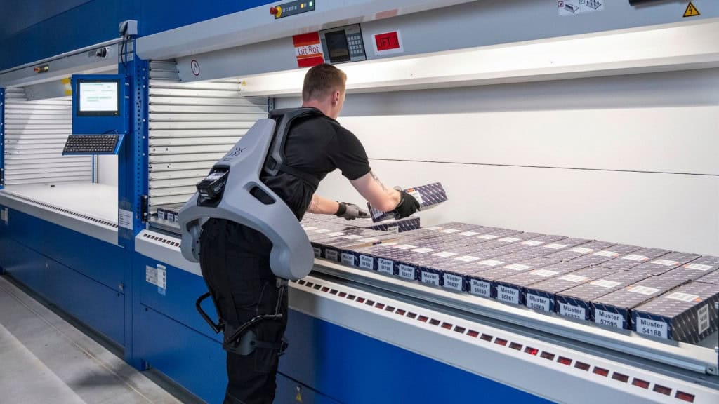 Homem de costas usando o exoesqueleto Exia, da German Bionic, manuseando um item numa esteira