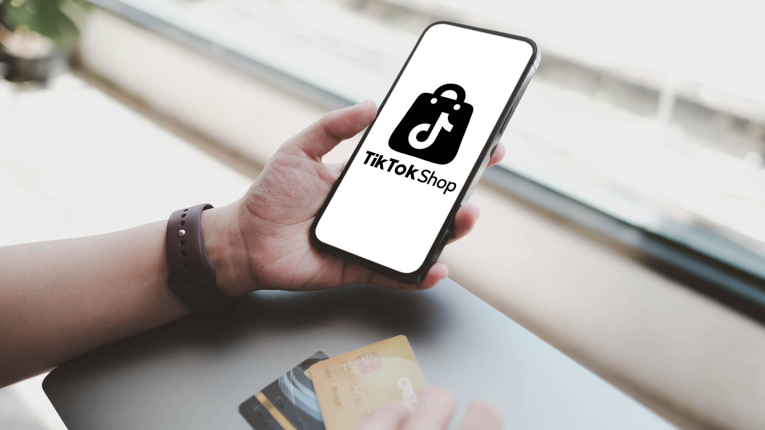 Pessoa segura com uma mão celular com logomarca da TikTok na tela enquanto segura cartões de crédito com a outra mão
