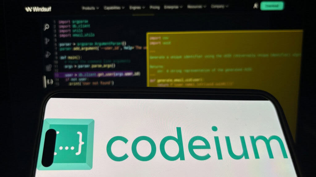 Celular exibindo nome e logotipo do Codeium; aparelho está na frente de tela exibindo software de programação da Windsurf