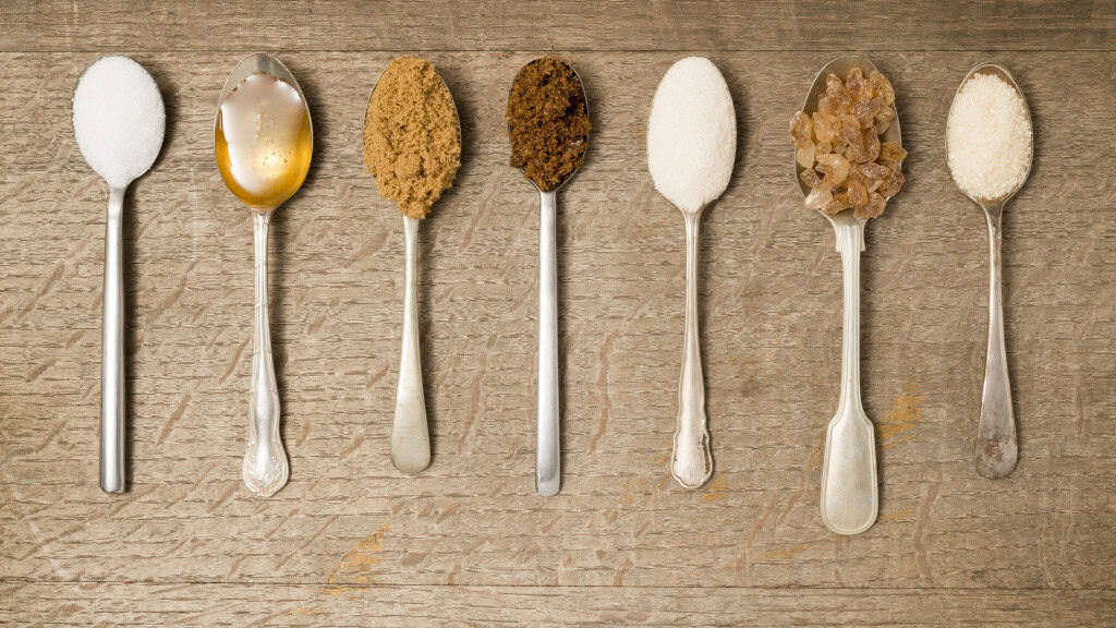 Sete colheres alinhadas com diferentes tipos de açúcar.