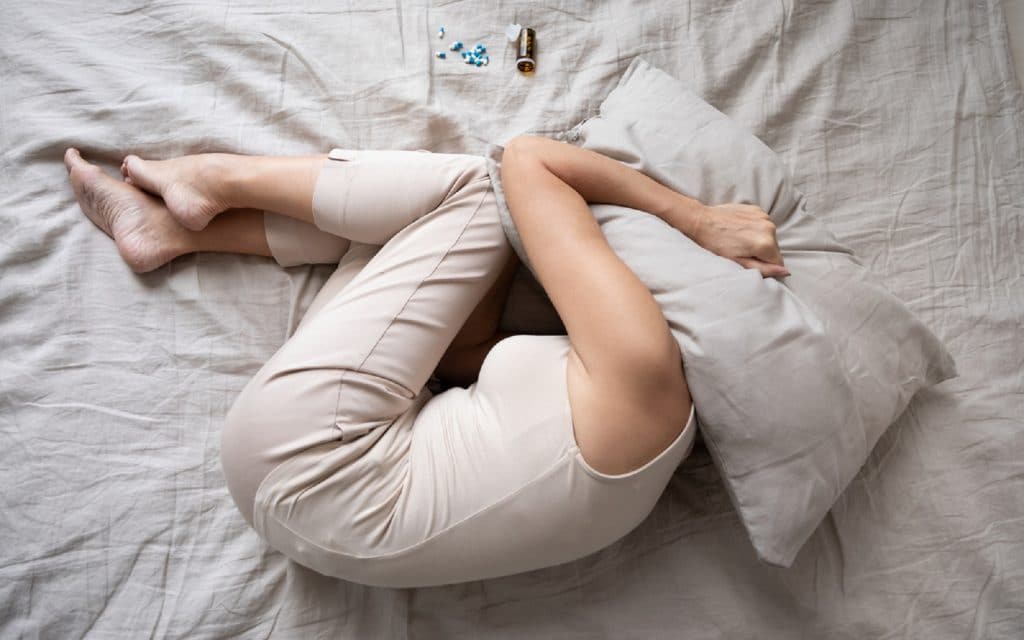 Mulher madura deprimida deitada na cama com frasco de comprimidos vista superior, cobrindo a cabeça com travesseiro