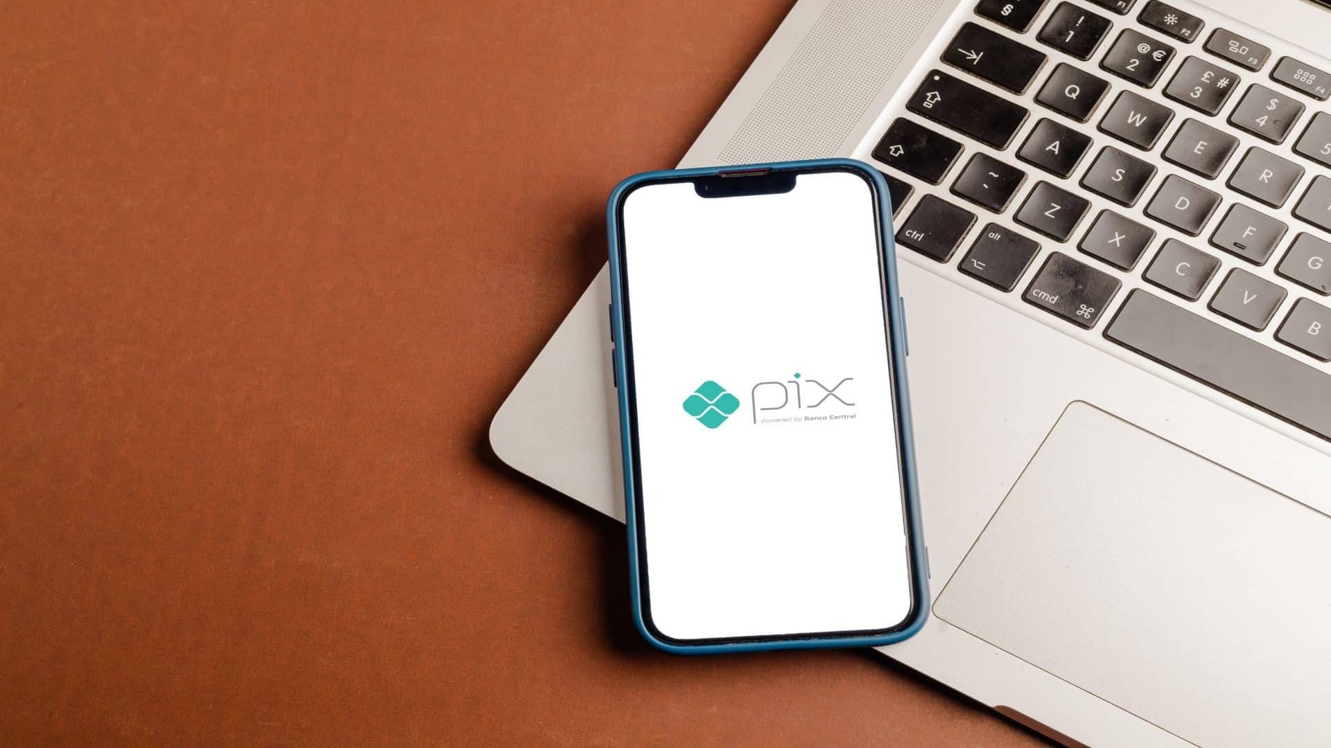 Imagem mostra celular mostra tela com logo do PIX, apoiado em laptop