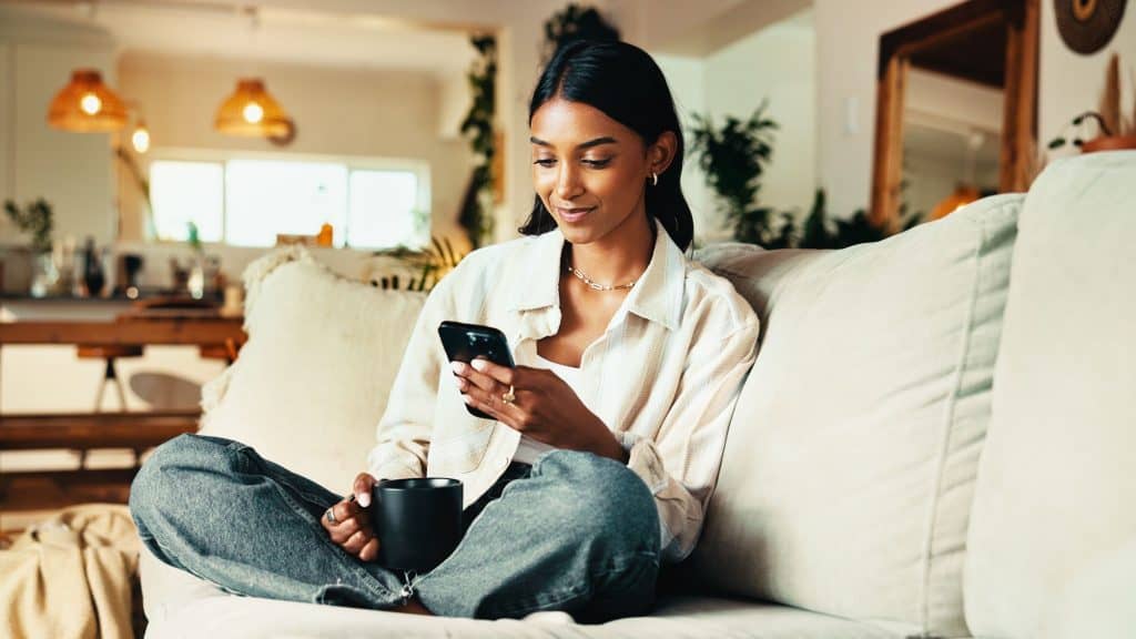 Mulher lendo e-book no smartphone sentada no sofá