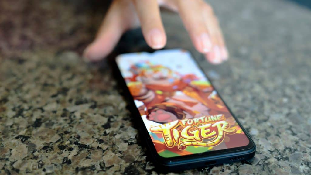 Mão estendida quase alcançando celular com jogo do tigrinho aberto