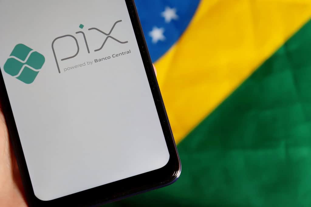 Ao fundo, bandeira do Brasil; à frente, smartphone exibindo, em sua tela, o logo do Pix