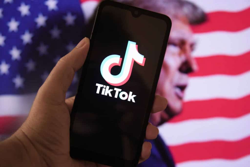 Ao fundo, bandeira dos EUA e imagem de Donald Trump; à frente, logo do TikTok em um smartphone